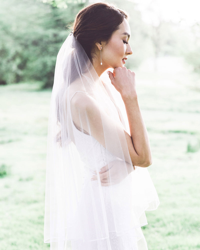 A bride wears the Teardrop Pearl Long Earrings, paired with a two-layer ribbon edge veil.