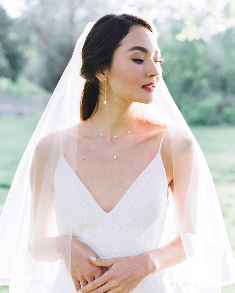 A bride wears the Teardrop Pearl Long Earrings, paired with a Layered Pearl Necklace and veil.