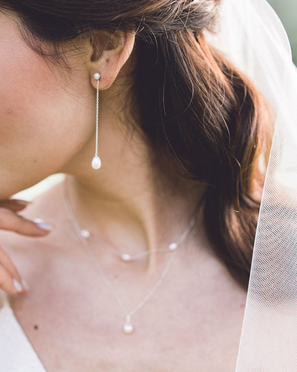 A bride wears a modern pearl jewellery set with Long Pearl Teardrop Earrings and a Layered Pearl Drop Necklace.