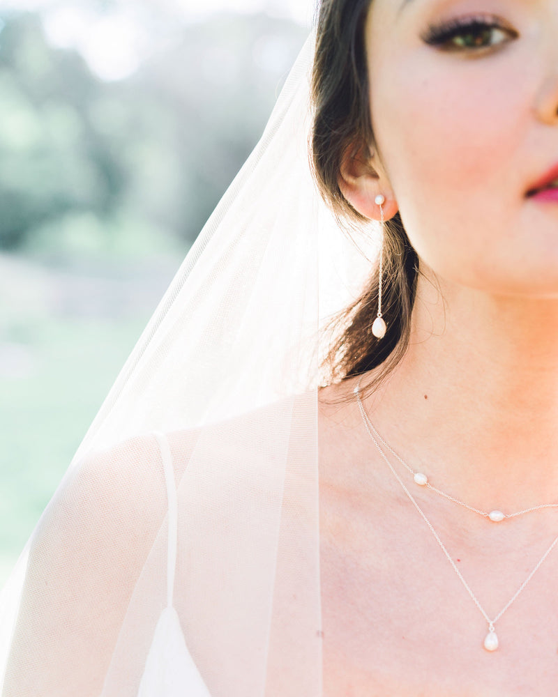 A bride wears a modern pearl jewellery set with Long Pearl Teardrop Earrings and a Layered Pearl Drop Necklace.