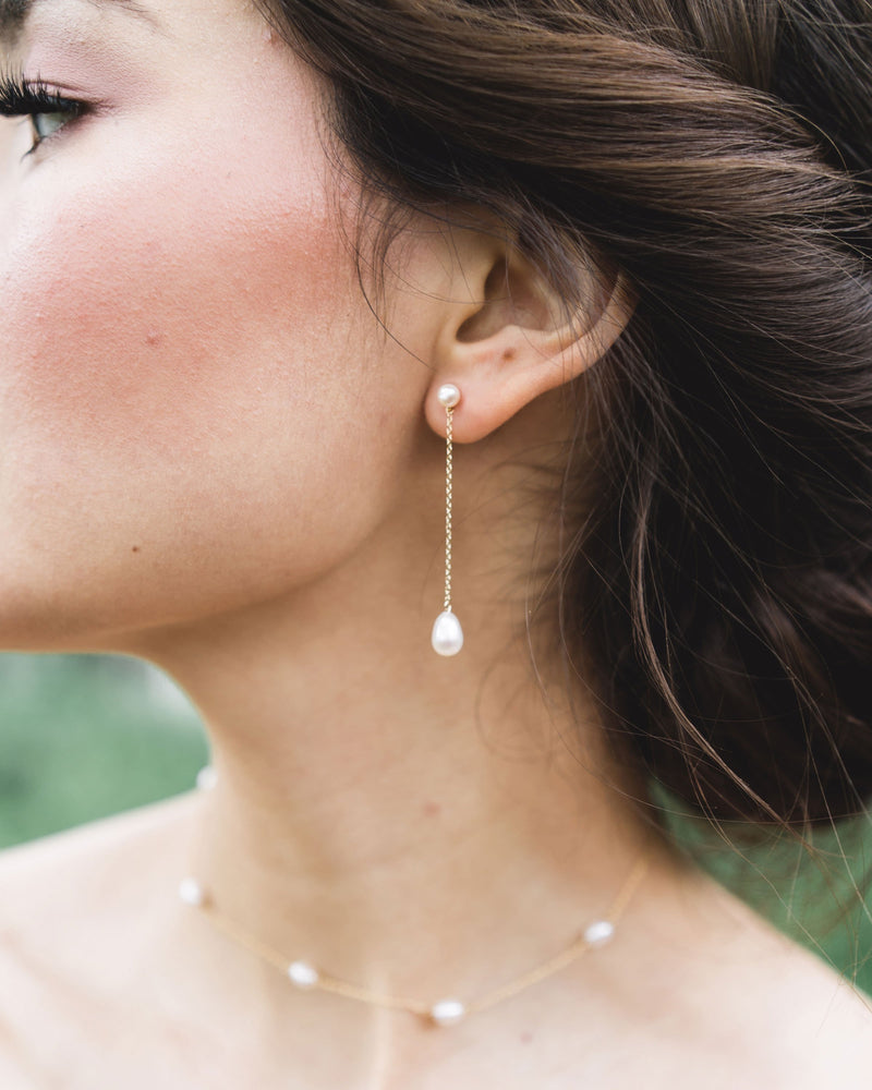A bride wears Teardrop Pearl Long Earrings, paired with a pearl station necklace.
