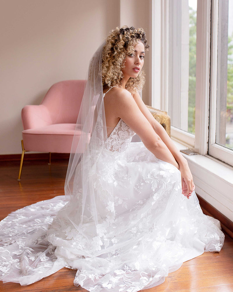 A bride sits prettily wearing the Wildflower Floral Lace Veil and a Made With Love bridal gown.