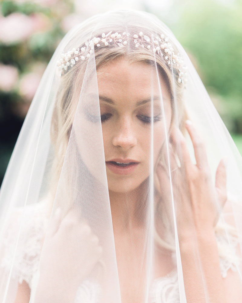 Close view of a bride wearing a pearl and crystal hair vine beneath a soft blusher veil.